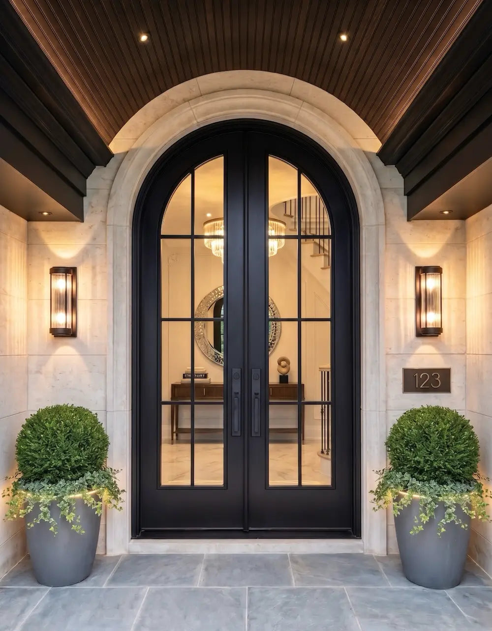 Decorative front door with glass panels flanked by two potted plants on a stone pathway.